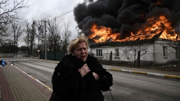 A woman stands in front of a house burning after being shelled in the city of Irpin, outside Kyiv, in March 2022