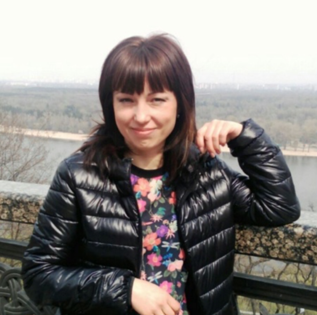 Женщина средних лет в черной куртке на фоне реки
